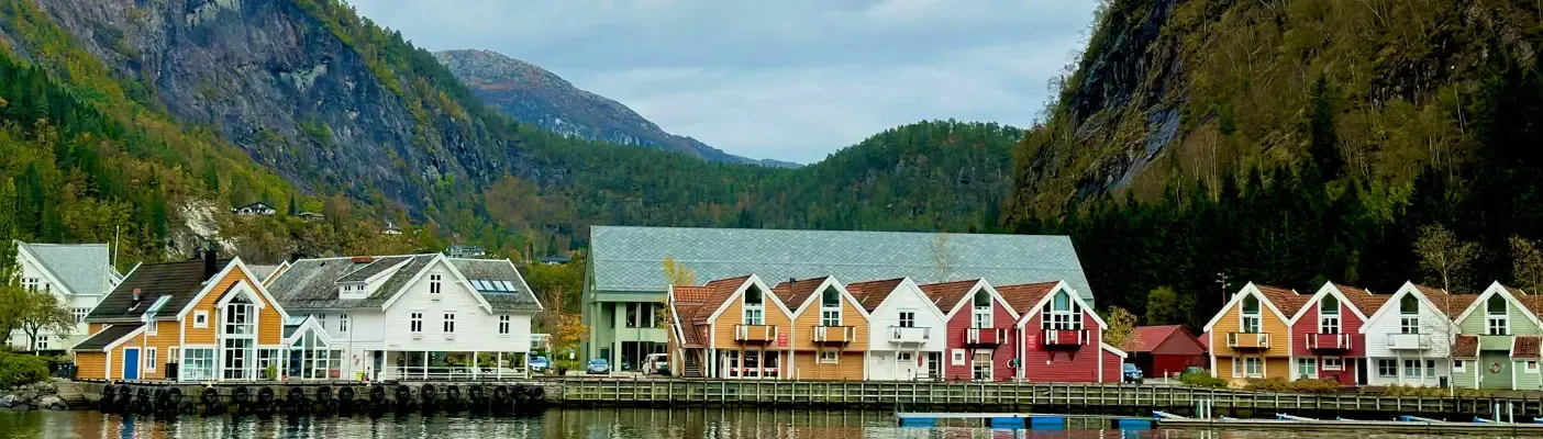 Kolorowe norweskie domki w malowniczym krajobrazie fiordów, otoczone górami i wodą. Widok idealnie oddaje klimat Norwegii.